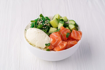Bowl with salmon, rice, chukka, cream cheese, cucumber, sesame seeds and pea sprouts on a white wooden background