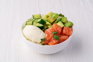 Bowl with salmon, rice, avocado cream cheese, cucumber and pea sprouts on a white wooden background