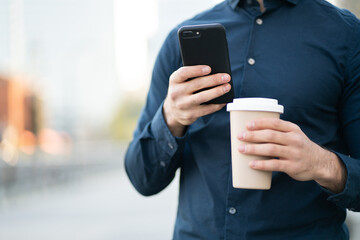 Man using his mobile phone and holding coffee outdoors.