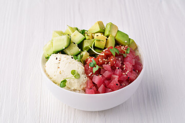 Bowl with tuna, rice, avocado cream cheese, cucumber and pea sprouts and sesame seeds on a white wooden background