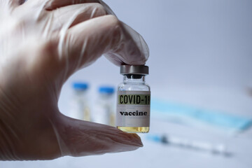 a gloved hand holds a bottle of coronavirus vaccine