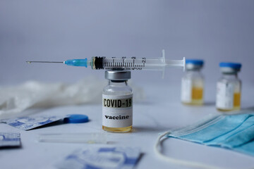 on the table is a bottle of coronavirus vaccine, on it is a syringe after the injection next to tot bubbles, mask and gloves