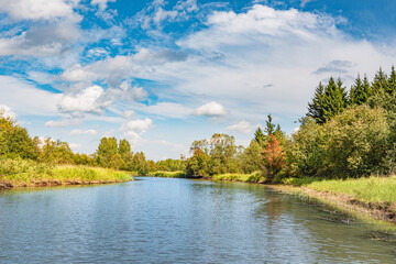 Panoramic landscape on a sunny day on the river with the sky in the clouds and the reflection in the water.