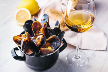 Mussels in a cauldron in a creamy sauce with croutons, lemon and a glass of white wine. Restaurant serving