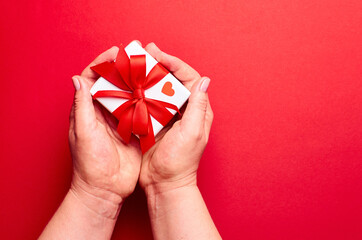 Hands holding gift box with small heart on red background