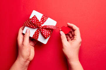 Women's hands holding gift box with small heart on red background