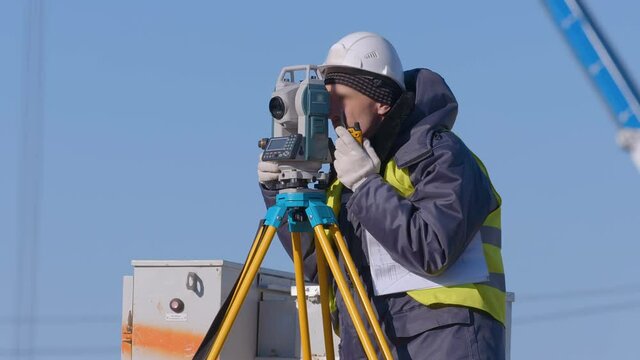 Surveyor with a theodolite doing his job, surveying the area for the construction of buildings and structures, for laying roads. He telling on walkie-talkie where to move the peg and fix the point  