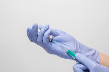 The Doctor draws the vaccine into the syringe. Hands with blue latex gloves.