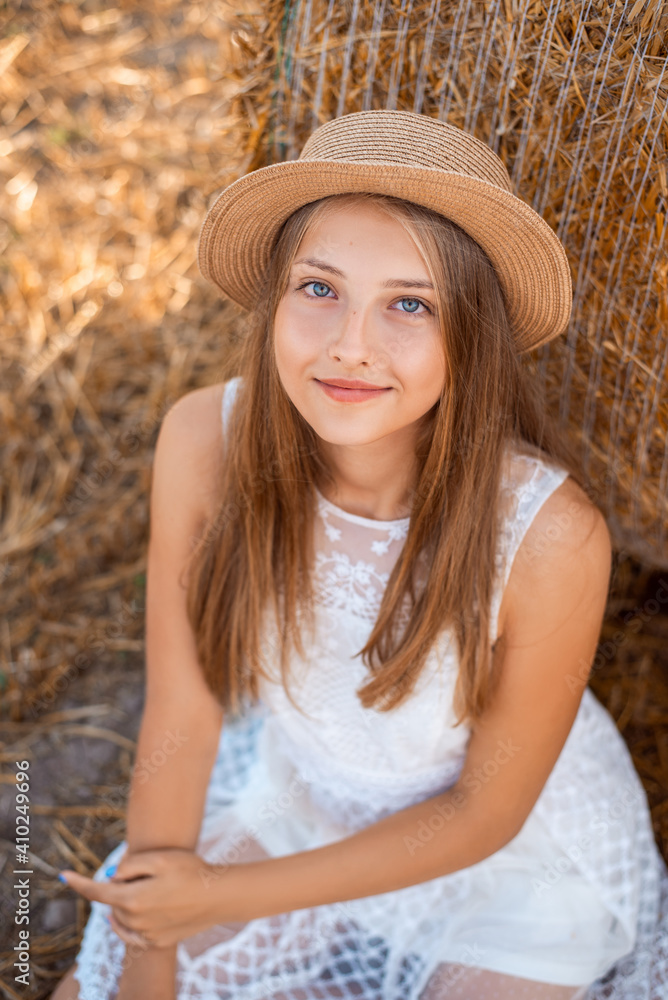 Canvas Prints Portrait of an attractive girl with a straw bale in the background. Outdoor photo of a beautiful girl