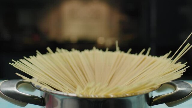 Male hand throwing spaghetti pasta into boiling water. Side view of pasta in pan in slow motion.