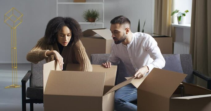 Focused confused couple young family african american wife and caucasian man open unpack parcel cardboard boxes look inside looking for important thing lost when moving to new home, search concept