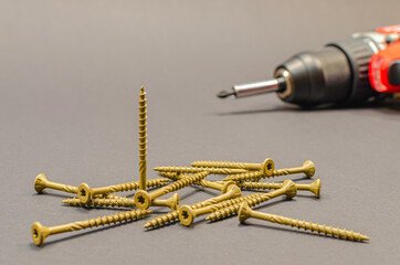 Self-tapping screws on the background of a battery screwdriver, a selection of different self-tapping screws on a black background