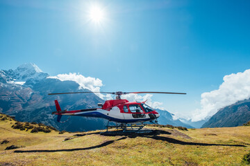 Fototapeta na wymiar Civil helicopter landed in high altitude Himalayas mountains. Thamserku 6608m mountain on the background. Namche Bazaar, Nepal. Safety air transportation and travel insurance concept image.