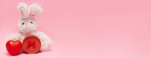 Fluffy bunny, hare with red heart and gift box on pink background. Valentines day concept banner with copy space