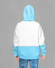 A young guy dressed in a blue and white hoodie with a hood on his head standing backwards