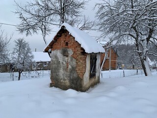 Old brick shed in the snow. Rural building in the yard. A covered house is a utility room.