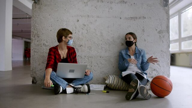 Young students with laptop sitting on floor back at college or university, coronavirus concept.