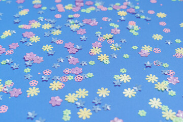 Fototapeta na wymiar Festive blue background with colorful flowers. Multi-colored small artificial flowers. Flat lay, top view.