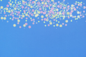 Festive blue background with colorful flowers with copy space. Multi-colored small artificial flowers. Flat lay, top view.