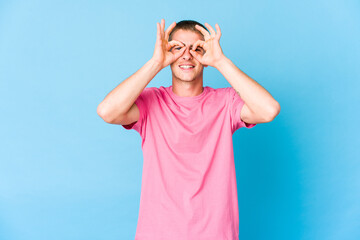 Young caucasian handsome man excited keeping ok gesture on eye.