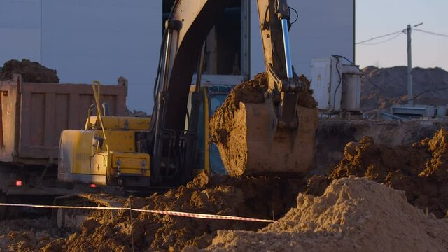 In winter, at a construction site, excavator remove a layer of earth to build the foundation of the future structure and load it into the bodies of dump truck 
