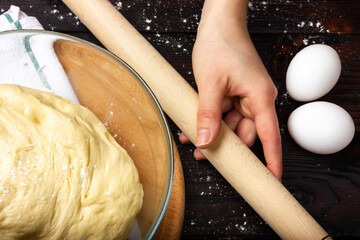 Rolling pin for rolling the dough in female hands. Cooking yeast dough. Dough for baking bread in a glass bowl.