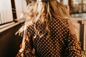 Outdoor close-up shot of back of curly blonde lady dressed in brown polka dot blouse © Look!
