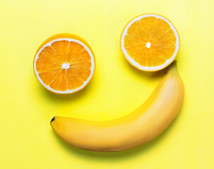 two orange slices and a banana on a yellow background. the figure looks like a smiley. joke concept...