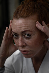 red-haired woman freckles 50 years old in white T-shirt worried and concentrated