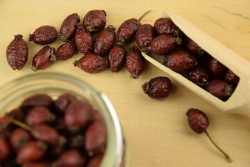 Rose hips, dried wild rose fruits on wooden spoon and on jar, natural wooden background, super food, healthy fruits, vitamin C and antioxidants resource