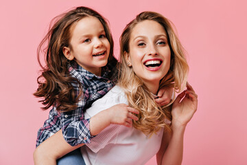 Close-up portrait of blonde, blue-eyed woman and curly little girl. Mom in white T-shirt and...
