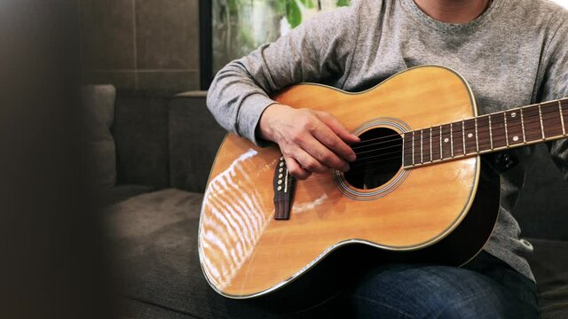 家のソファに座ってギターを練習する日本人の男性