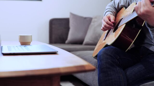 家のソファに座ってギターを練習する日本人の男性