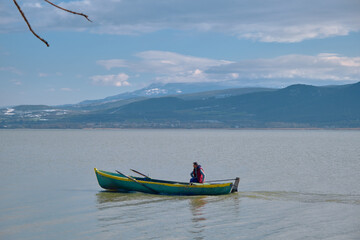 Man on small and old boat at the lake of Uluabat with huge mountain backgrounds. Golyazi. Bursa. Turkey. 22.01.2021