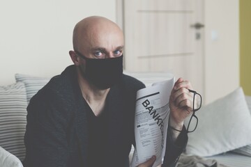 Sad and depressed businessman in a protective mask shows the signed bankruptcy document. Sadness...