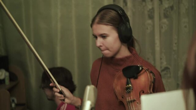 Woman rehearsing melody with violin using headphones under mentorship by teacher
