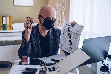 Sad and depressed businessman in a protective mask shows a signed bankruptcy document. Bankruptcy...