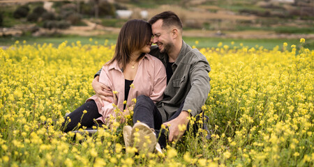 Fototapeta premium young happy couple sitting in the field with flowers