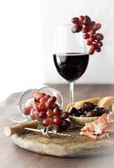 A wine glass filled with red wine and red grapes on a rustic charcuterie board.