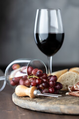 A glass of red wine with another wine glass tipped over with red grapes spilling out on a rustic...