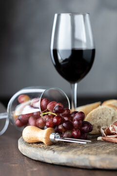 A Glass Of Red Wine With Another Wine Glass Tipped Over With Red Grapes Spilling Out On A Rustic Board.