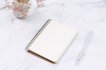 Open notebook, plant and pen on marble surface. Blank page for notes.