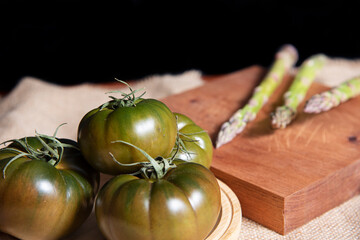 Fresh and organic green tomatoes and some asparagus, on a wooden table.