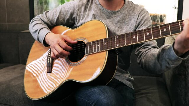 家のソファに座ってギターを練習する日本人の男性