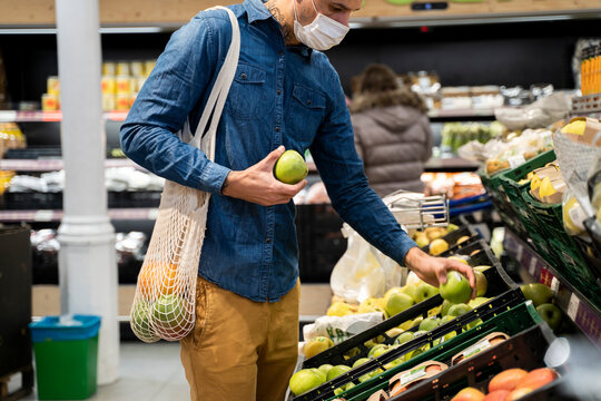 Midsection of man wearing face mask buying granny smith apples in supermarket