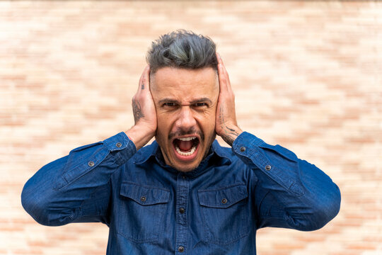 Frustrated man covering ears while shouting against wall