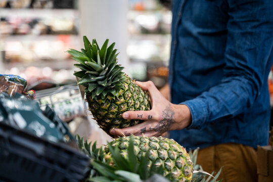 Midsection of mid adult man buying pineapple in supermarket