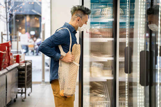 Stylish man looking in display cabinet at supermarket