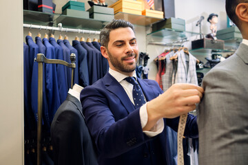 Tailor in his menswear store taking customers measurements for suit