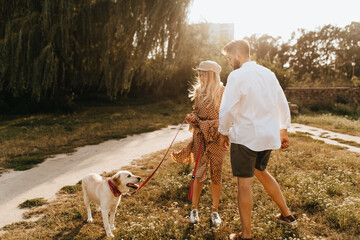 Full-length portrait of young married couple walking dog in park on sunny day